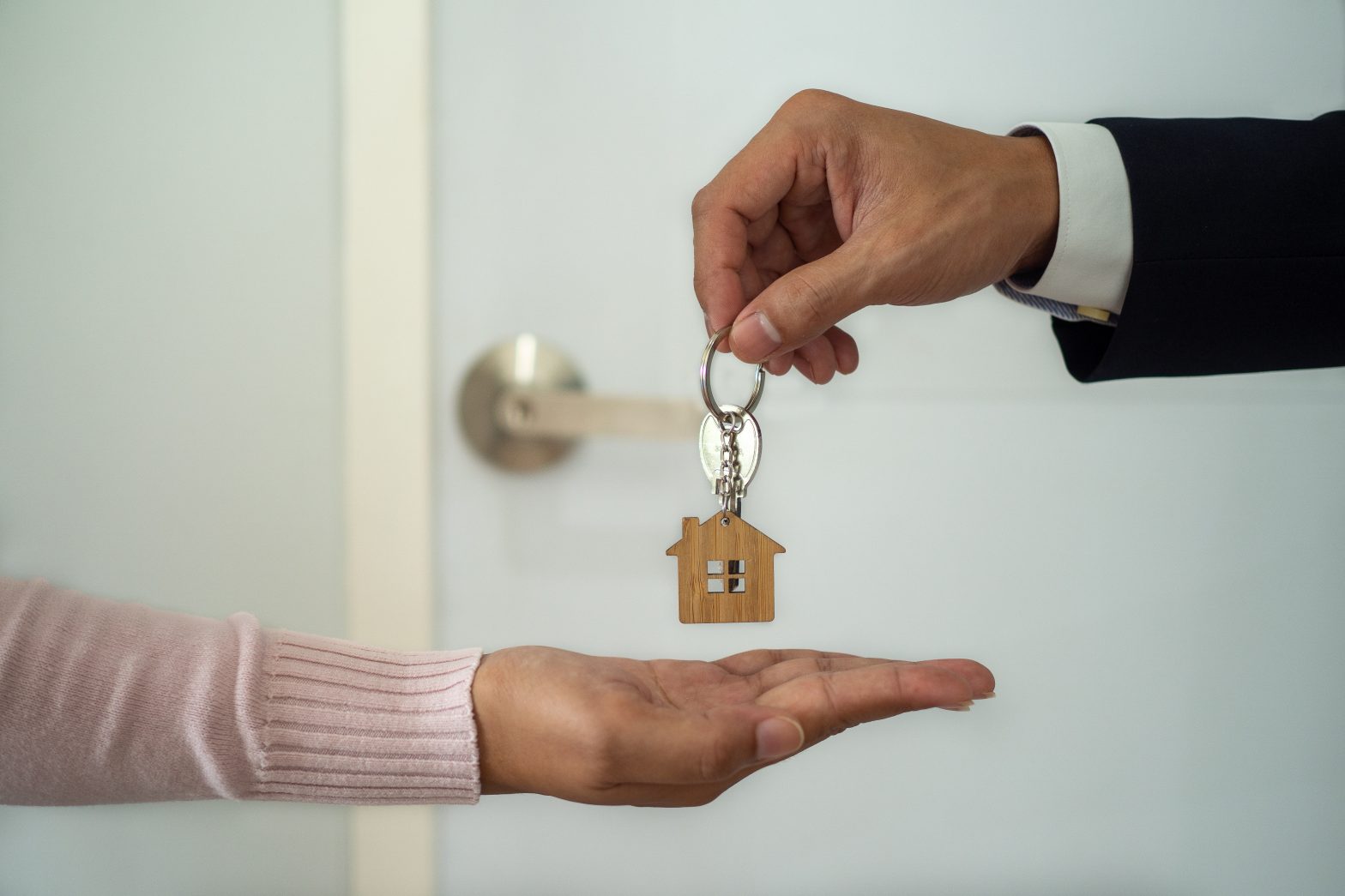 The business man in the suit giving a house key to the woman's hand. Employees sending a new home keys to buyers. concept of Landlords or buying and selling real estate rentals
