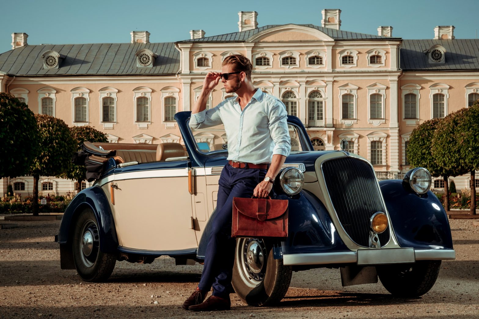 Confident wealthy young man with briefcase near classic convertible.