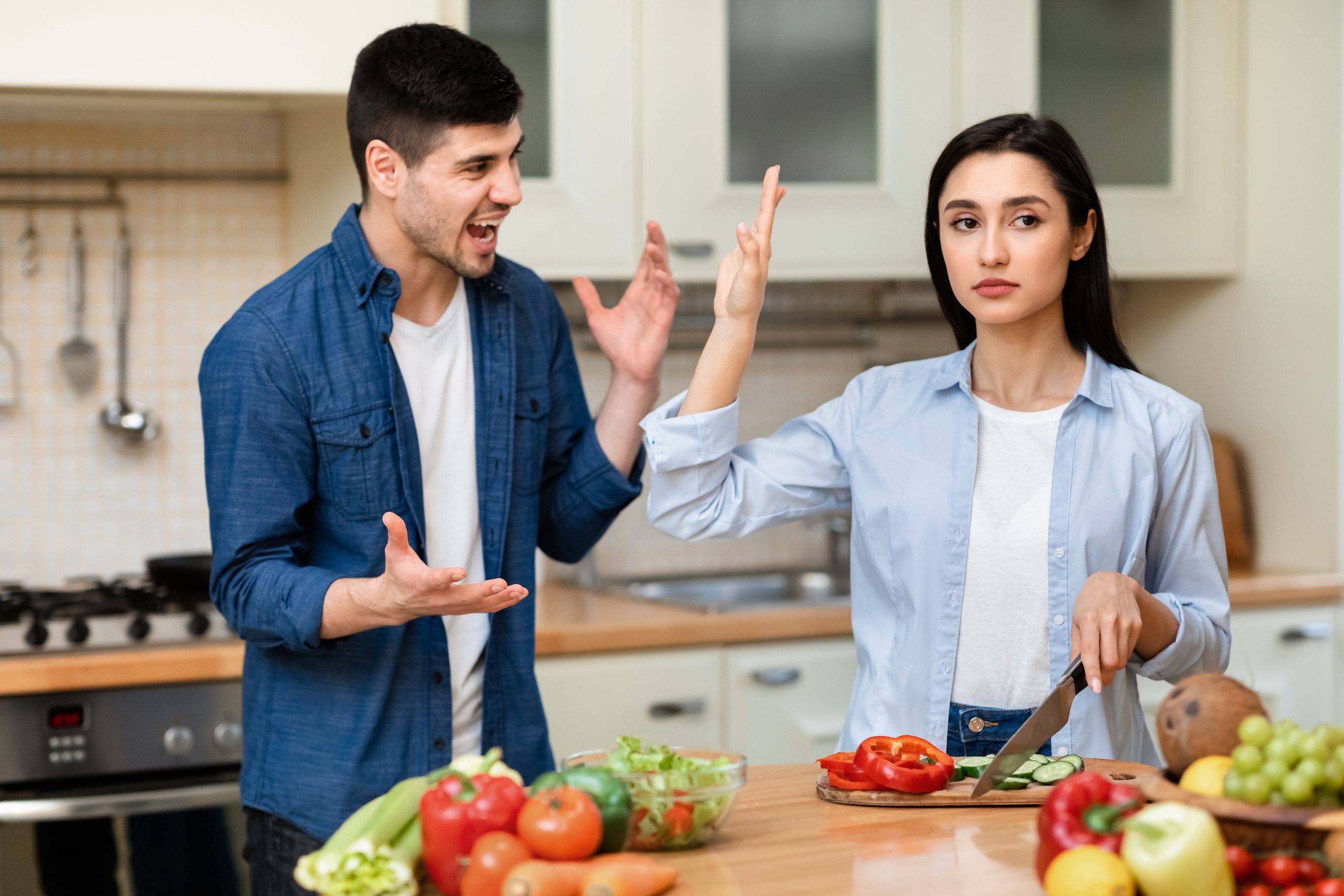 Young couple arguing in the kitchen, man screaming, woman stopping him, showing palm