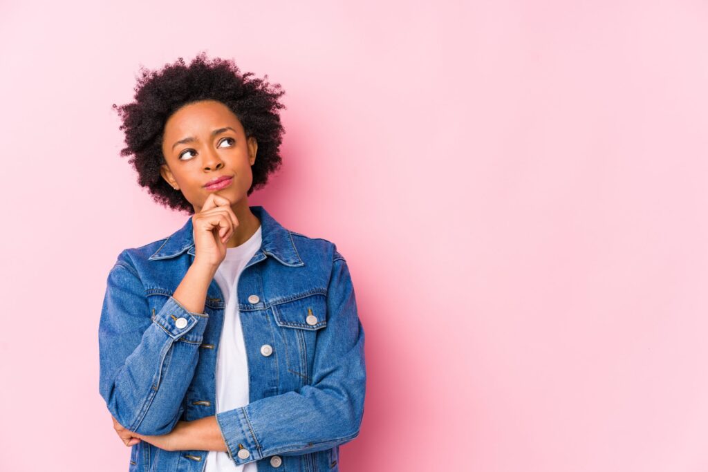 Young woman against a pink backgroound isolated looking sideways with doubtful and skeptical expression.