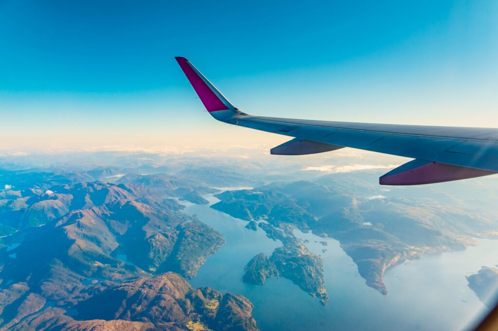 View from an airplane to jet wing and norwegian fjords landscape. Aircraft flying over Norway Scandinavia.