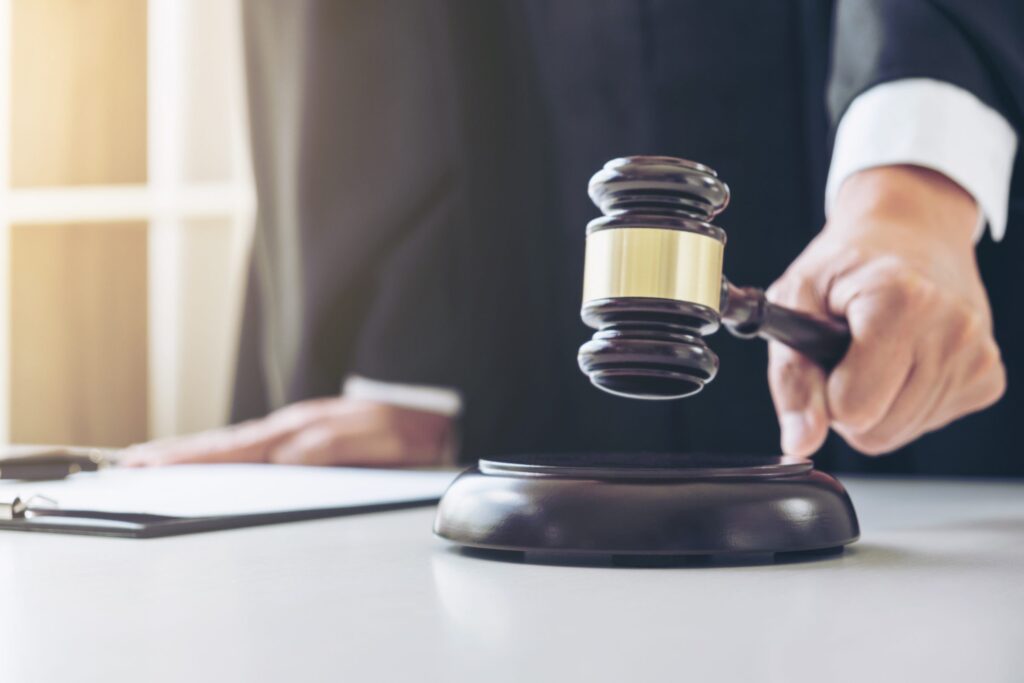 Close up of Male lawyer or judge hand's striking the gavel on sounding block, working with Law books, report the case on table in modern office, Law and justice concept.