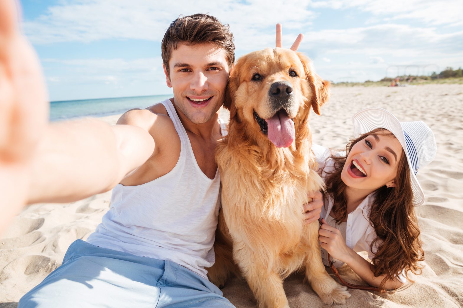 Young happy couple with dog taking a selfie at the beach