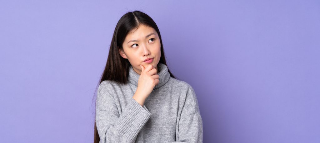 Young asian woman over isolated background having doubts