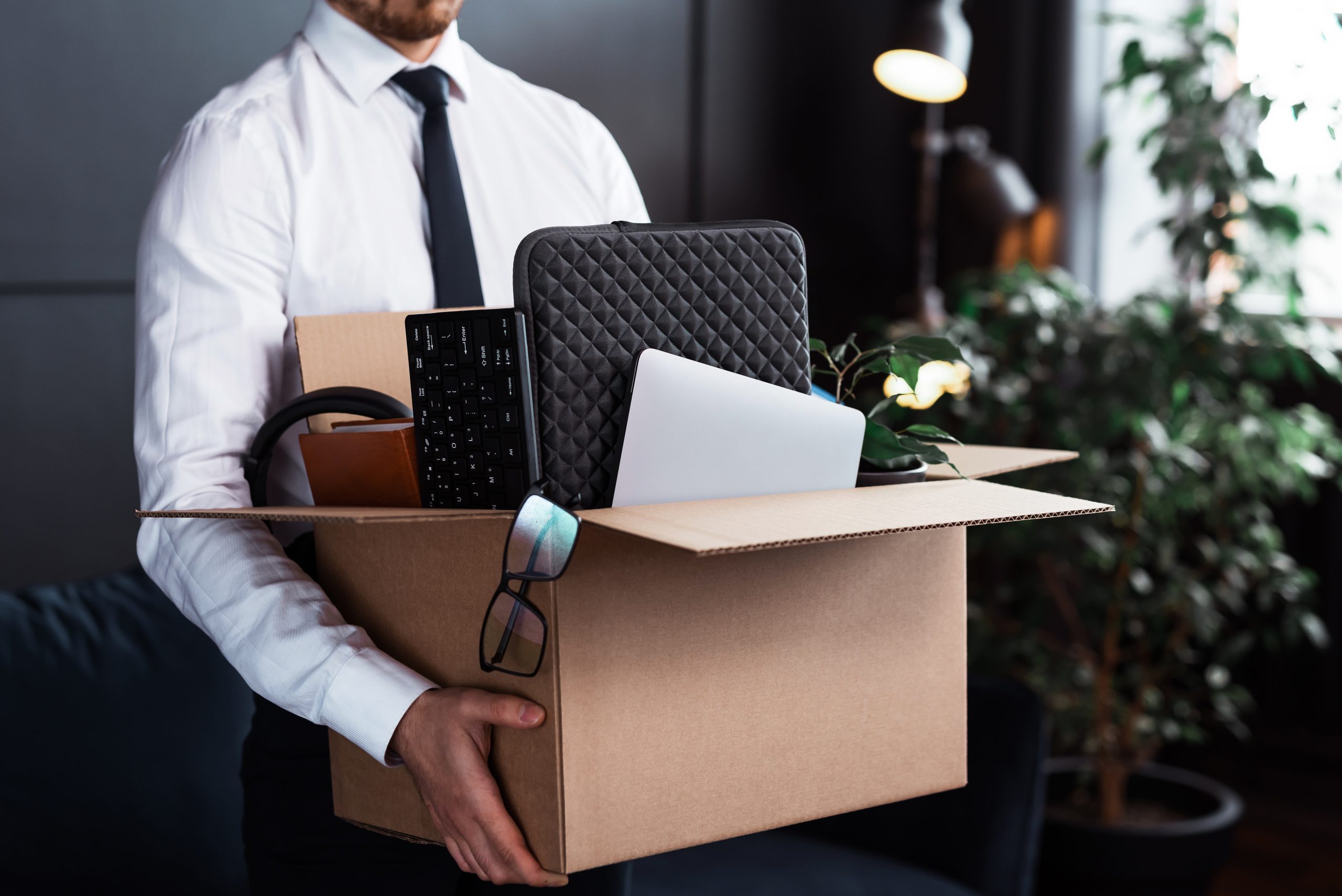 Young man getting fired from his job. Businessman and cardboard box with his personal stuff from work.