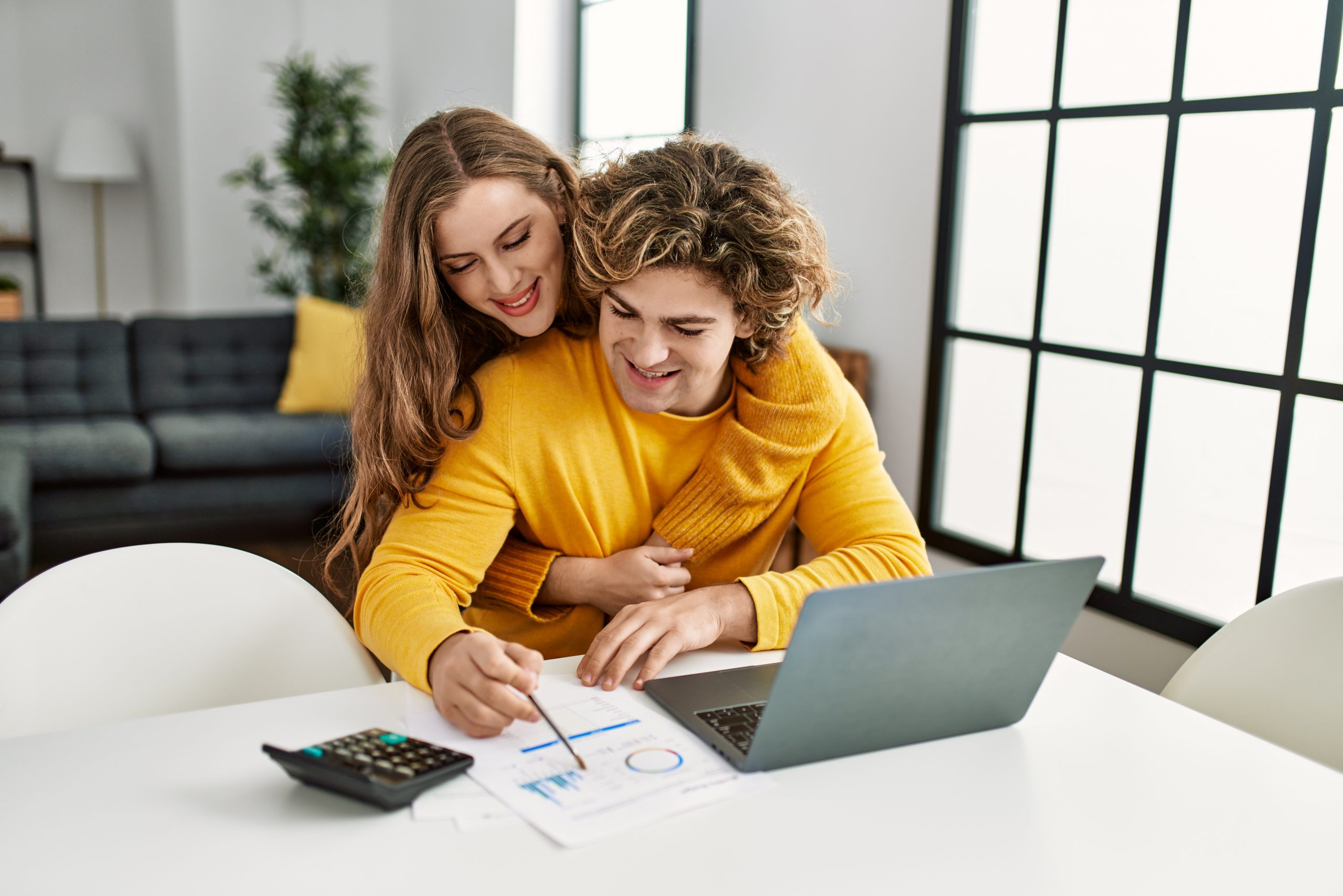 Young caucasian couple hugging each other doing family accounting using laptop at home