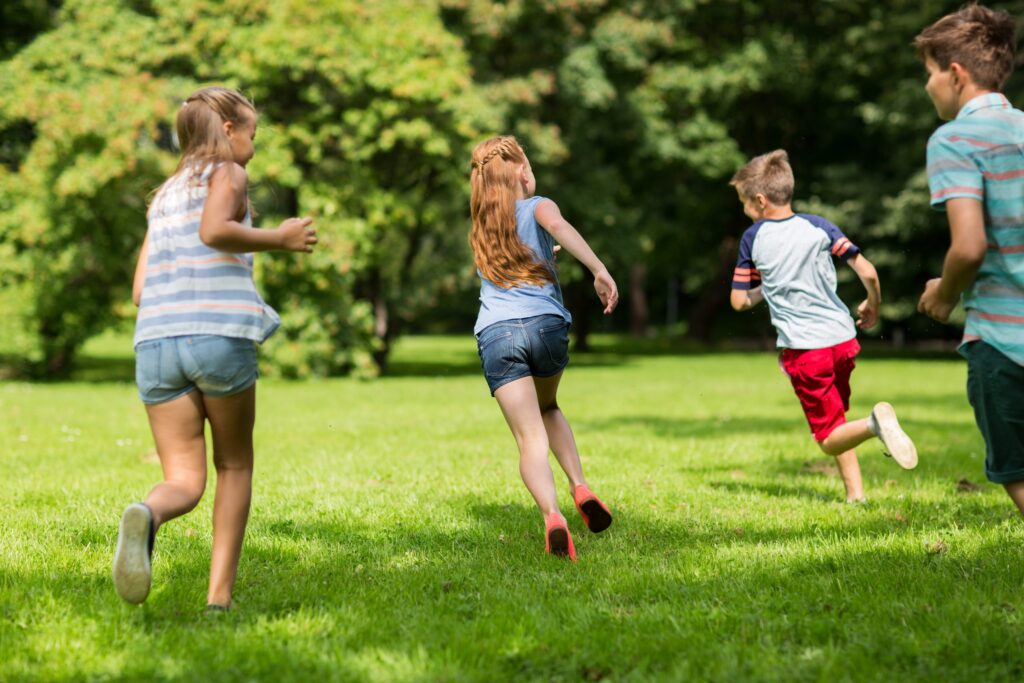 friendship, childhood, leisure and people concept - group of happy kids or friends playing catch-up game and running in summer park