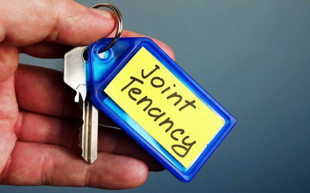 Hand holds key with Joint Tenancy inscription.