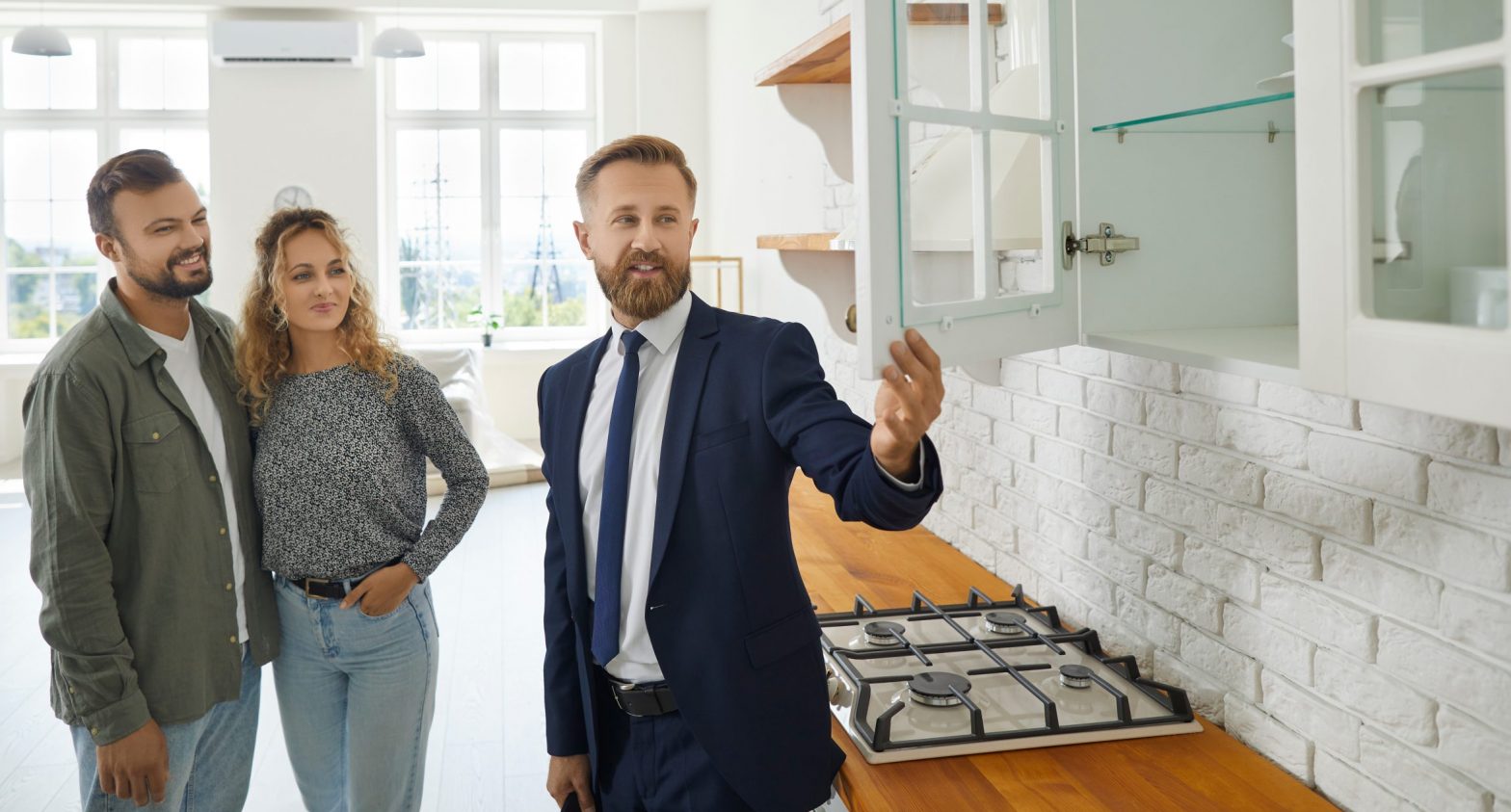 Real estate agent giving first time buyers or future tenants tour about new home. Boyfriend and girlfriend buying modern house.Husband and wife consulting expert on good quality wooden kitchen cabinet