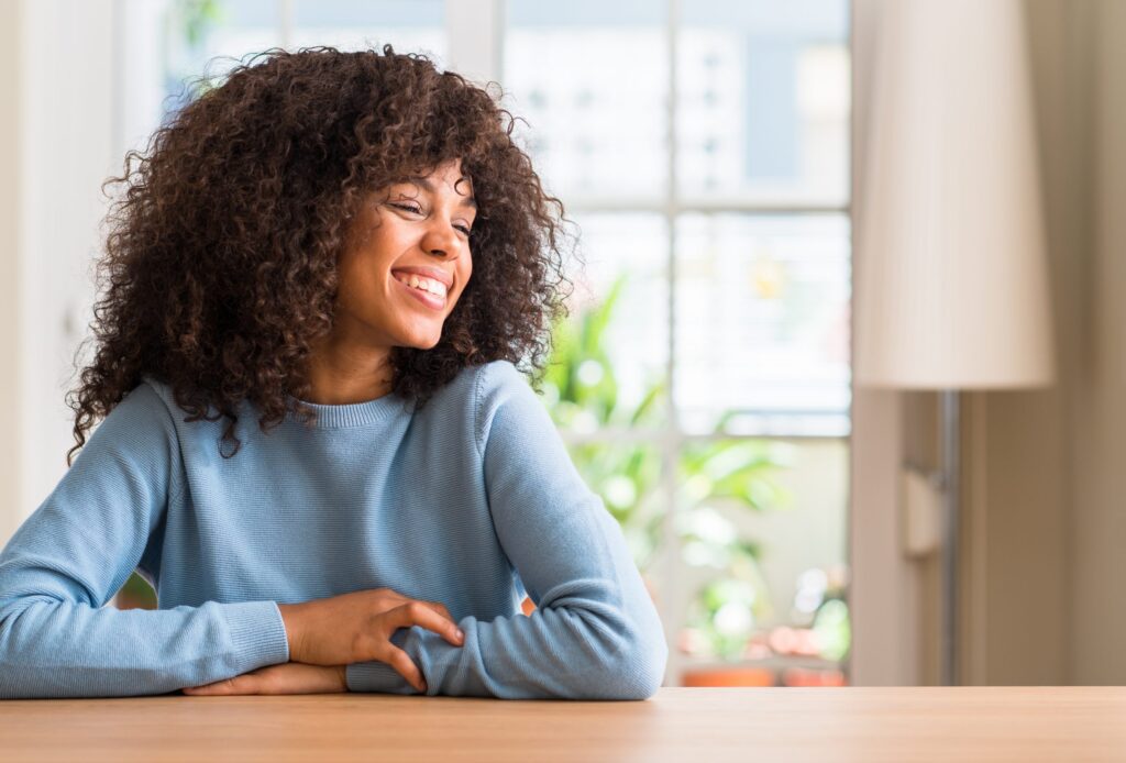Black woman at home looking away to side with smile on face, natural expression. Laughing confident.