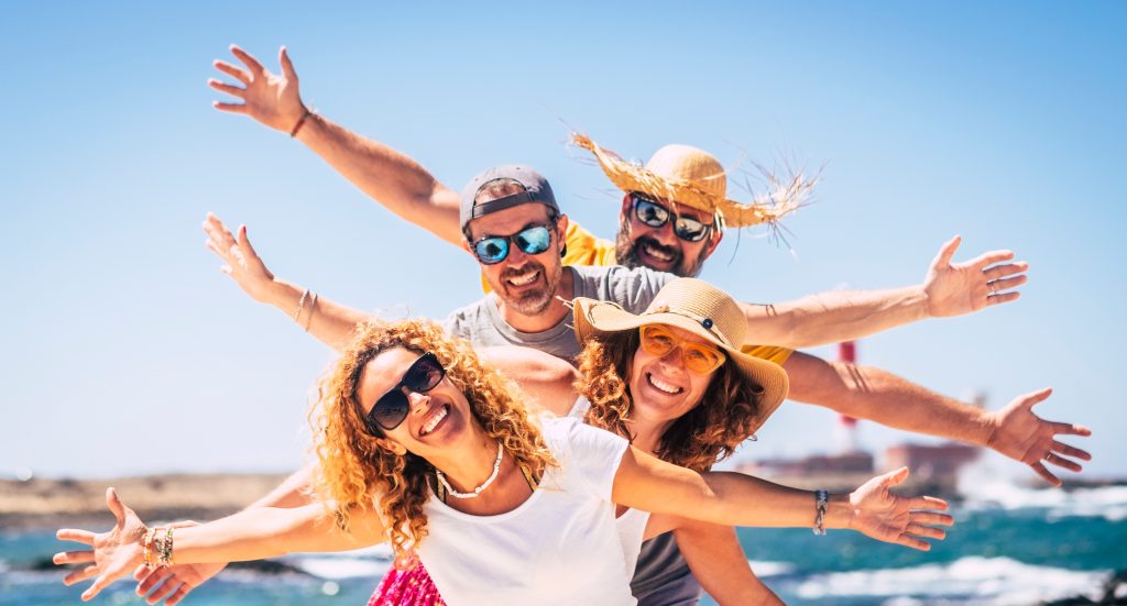 Group of happy people enjoy travel and summer holiday vacation together having fun under the sun - blue ocean water in background and sky - joyful adults smile with cheerful expressions