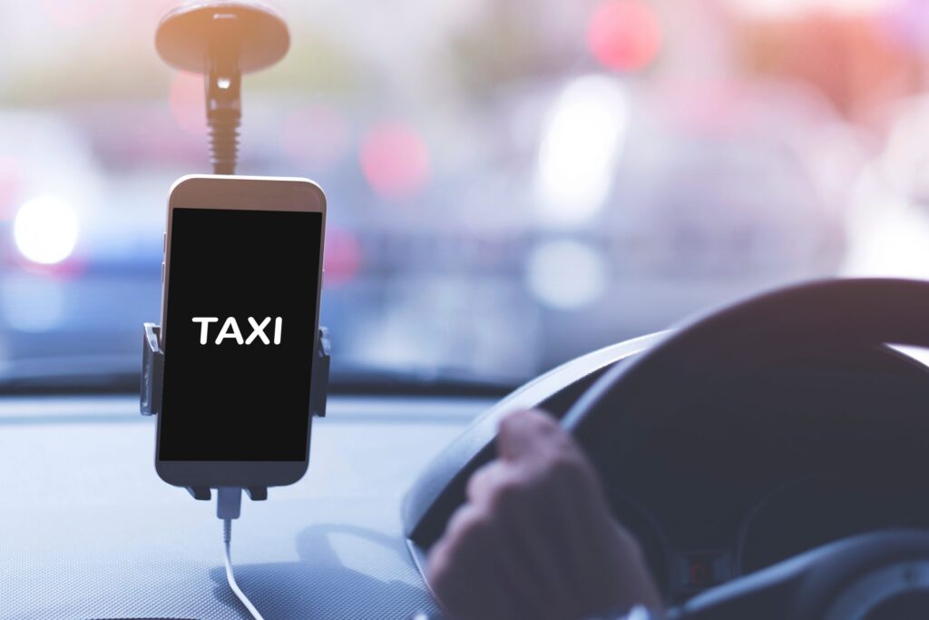 An unidentified man driving an Uber. Image taken from back seat with taxi word on phone screen.