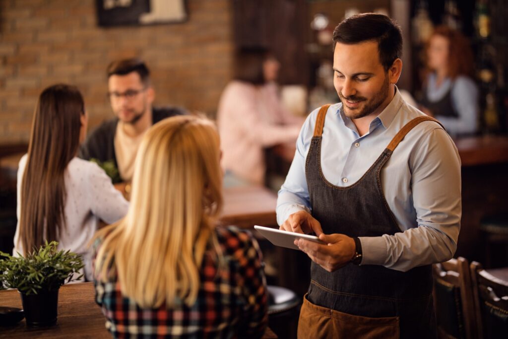 Smiling waiter talking to a woman while taking her order on digital tablet in a bar.