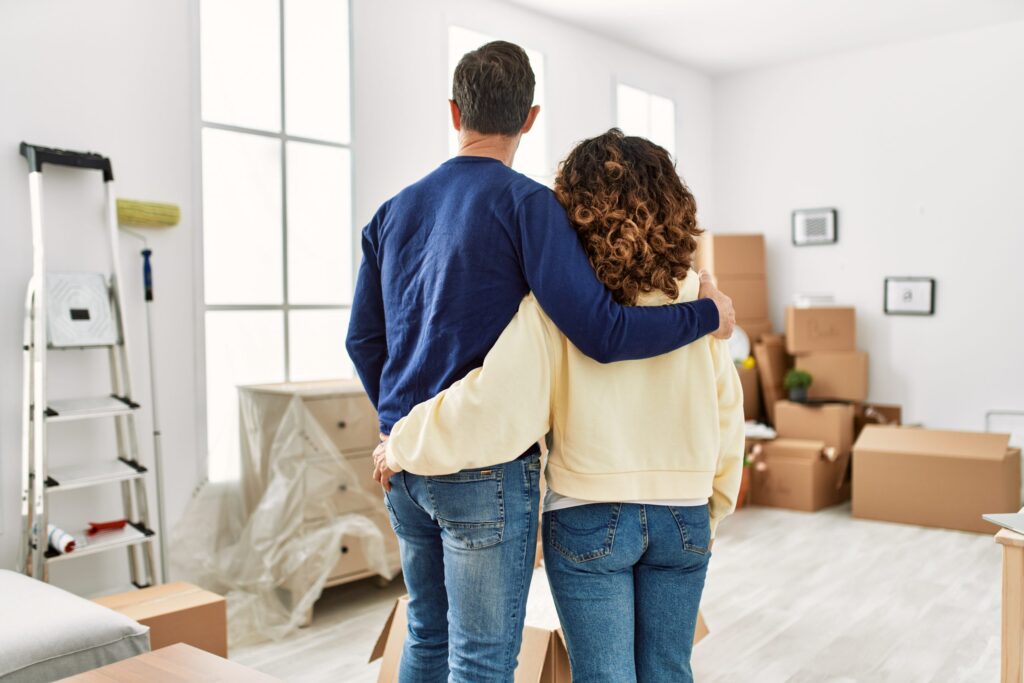 Middle age hispanic couple on back view hugging and standing at new home.