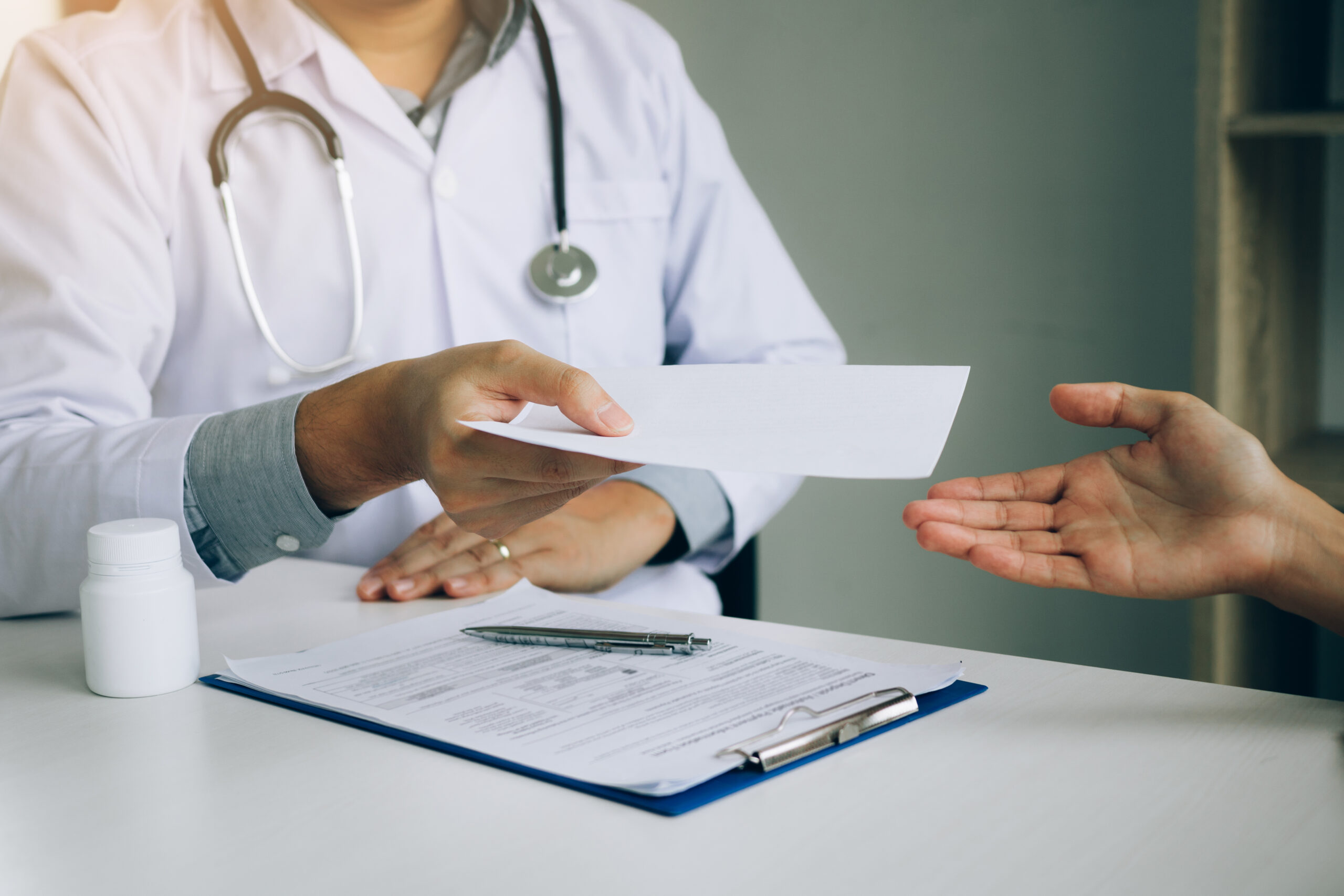 Asian male doctor talking in clinic room and handing a prescript