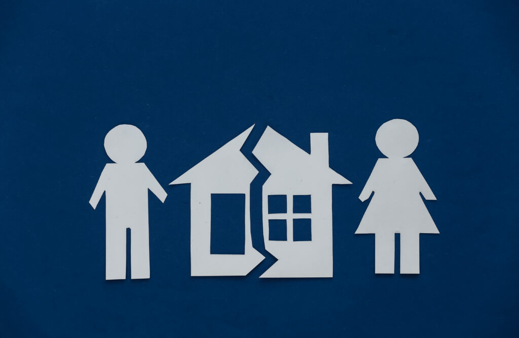 The concept of separation of property divorce Half-cut paper house and figures of man and woman on classic blue background