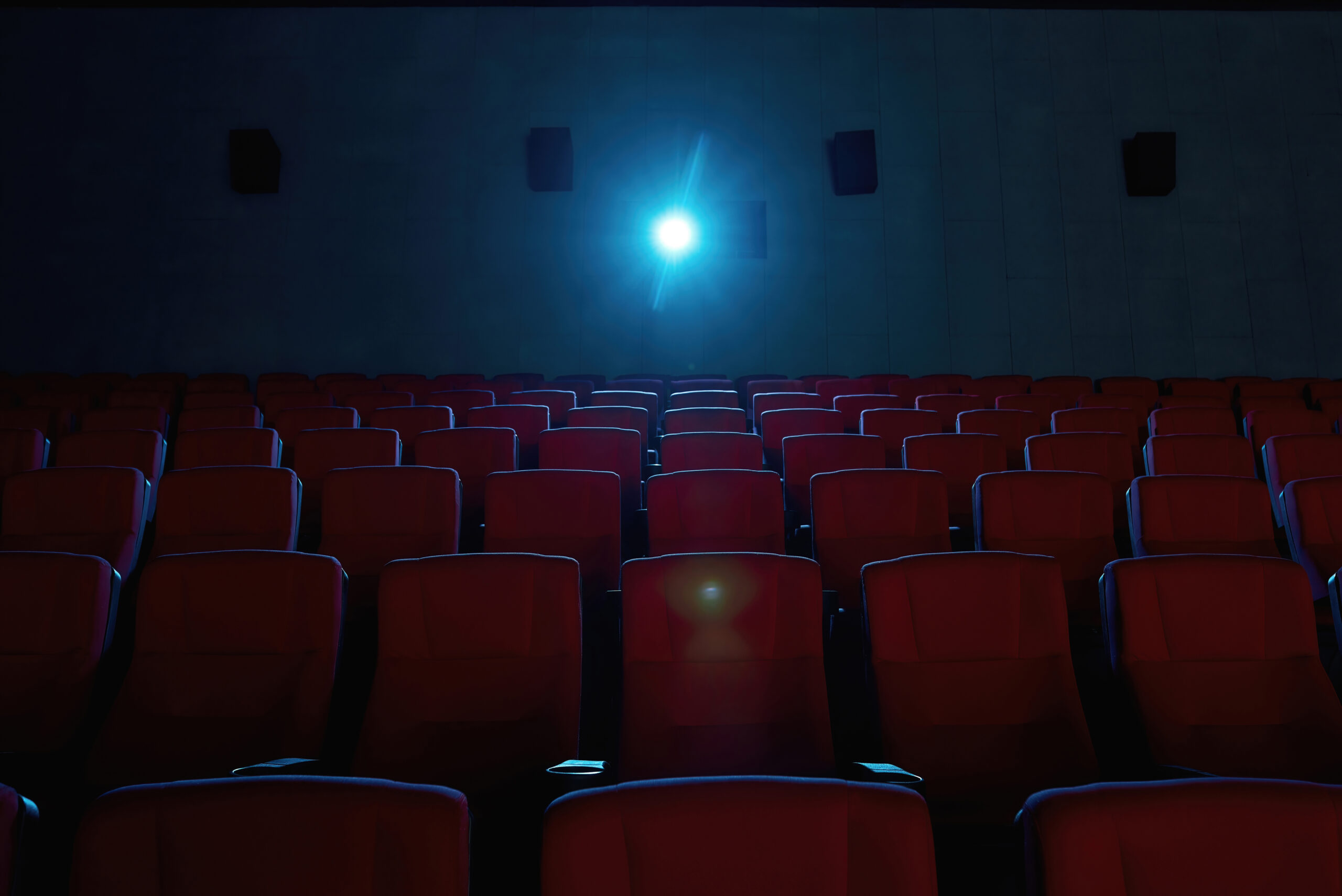 Interior of movie theater with empty red seats and projector