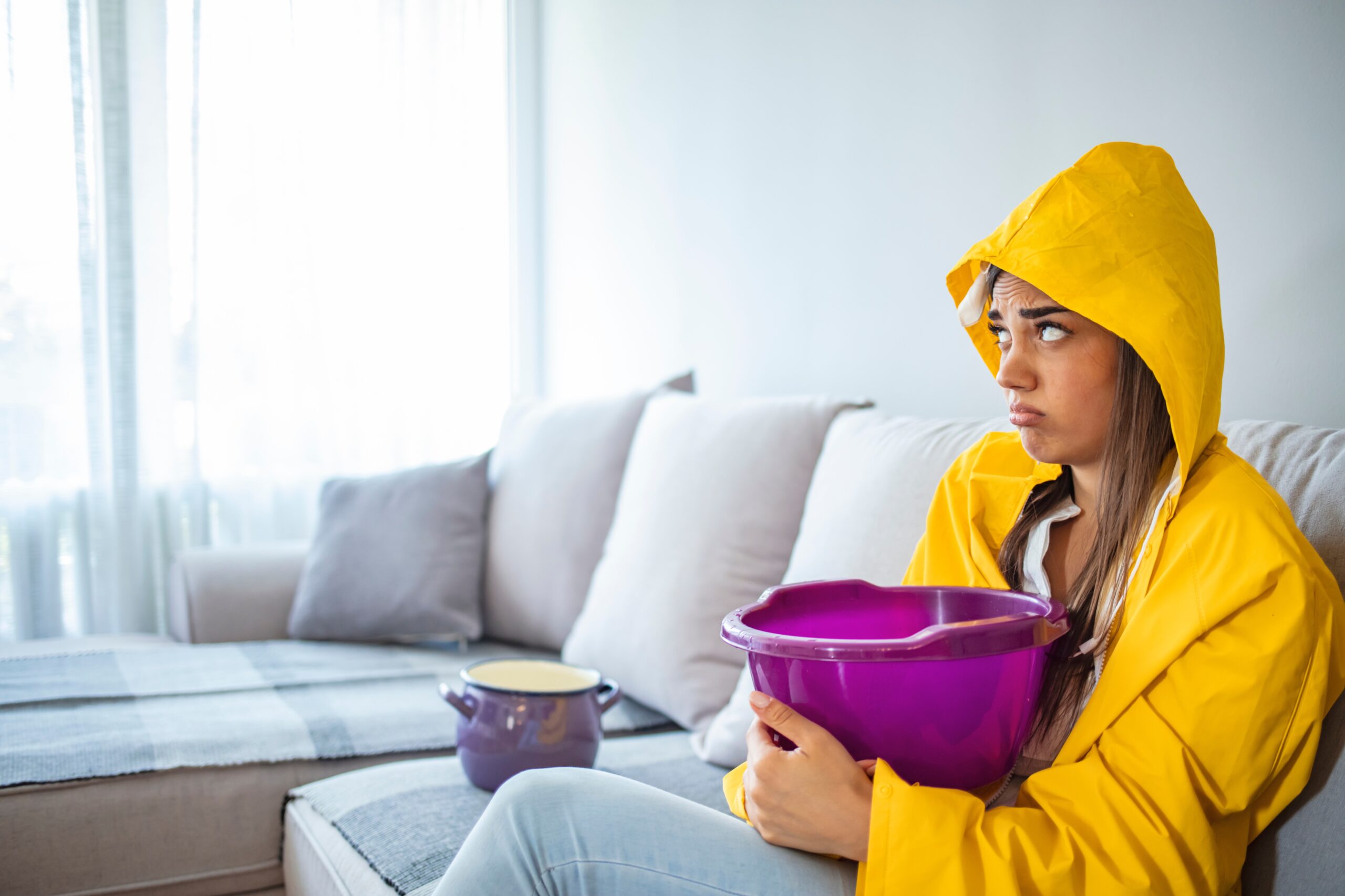 Women in raincoat holding bucket due to roof leak