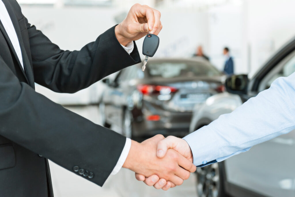 Car dealer shaking hand with buyer and holding car keys