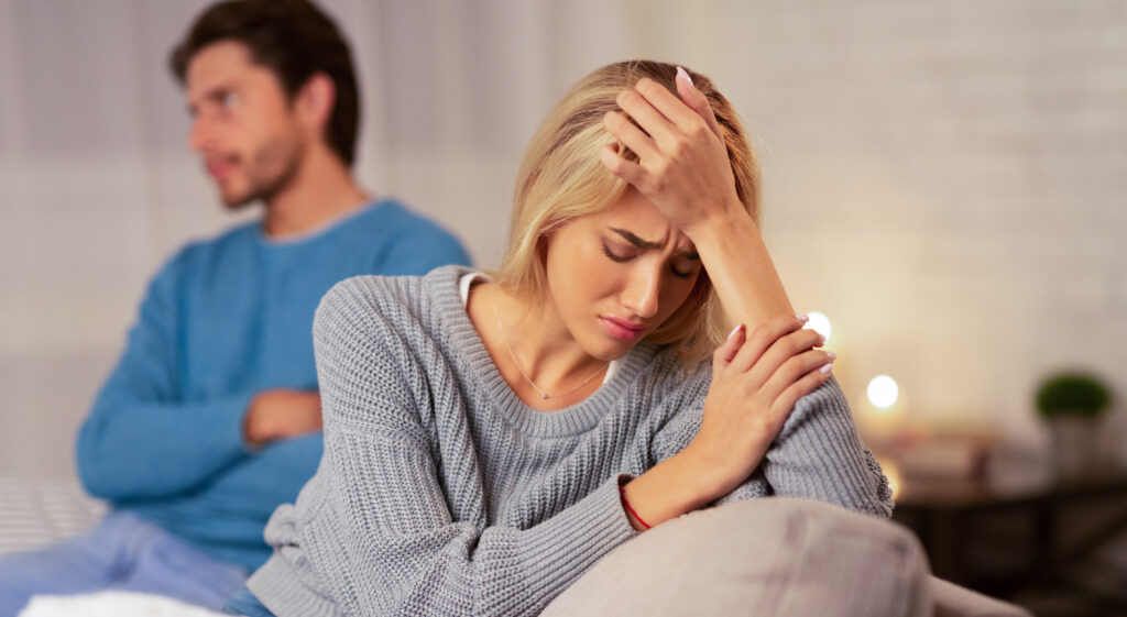 Depressed Wife Sitting Next To Indifferent Husband At Home