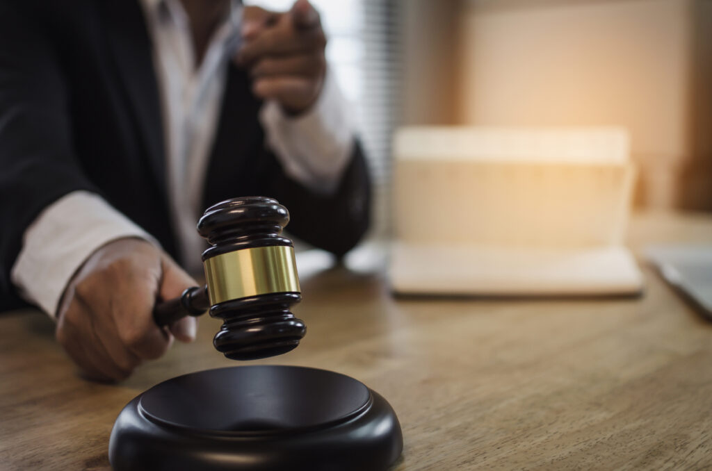 justice lawyer in black suit pointing finger and knocking wooden judge gavel with documents on workplace desk in courtroom office occupation business justice law and legal service concept