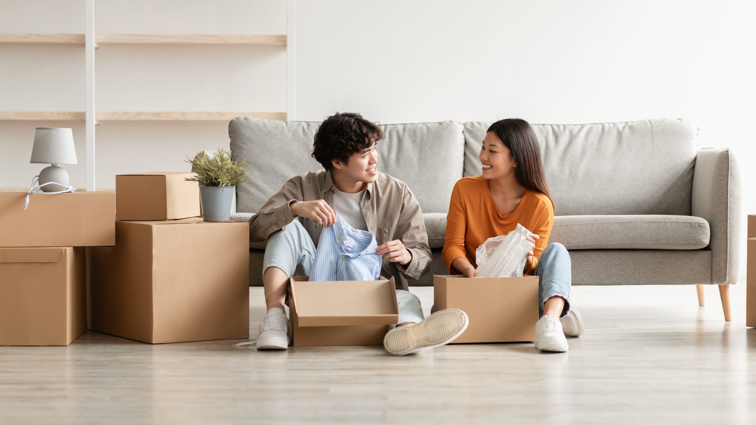 Cheerful Asian couple unpacking belongings and having conversation moving to new apartment or their own house