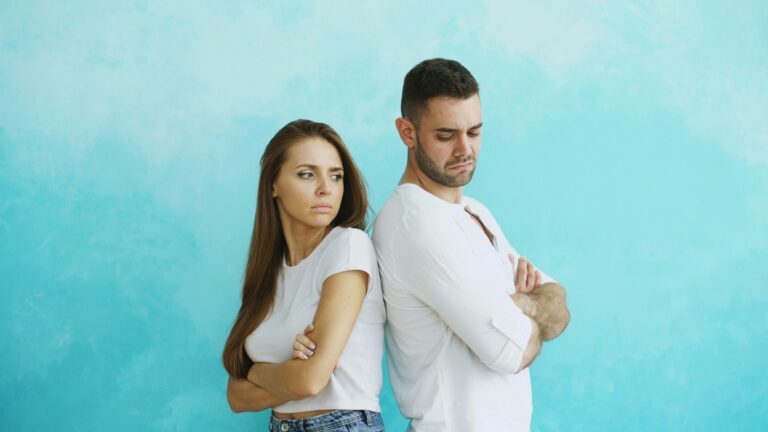 Young couple upset and angry each other standing back to back on blue background