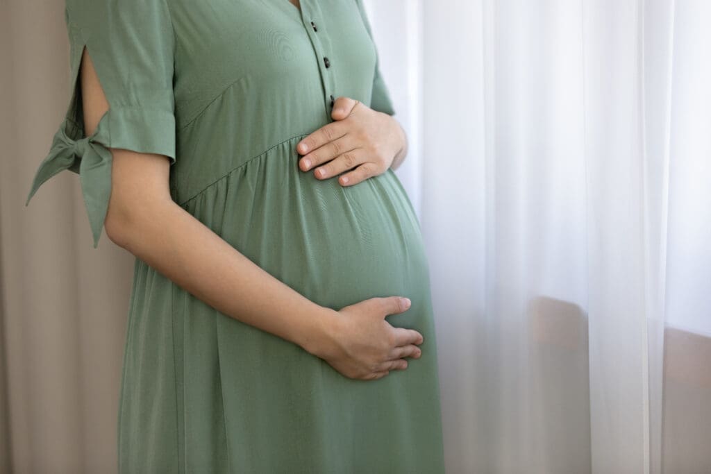 Tender single pregnant woman embrace big tummy by window