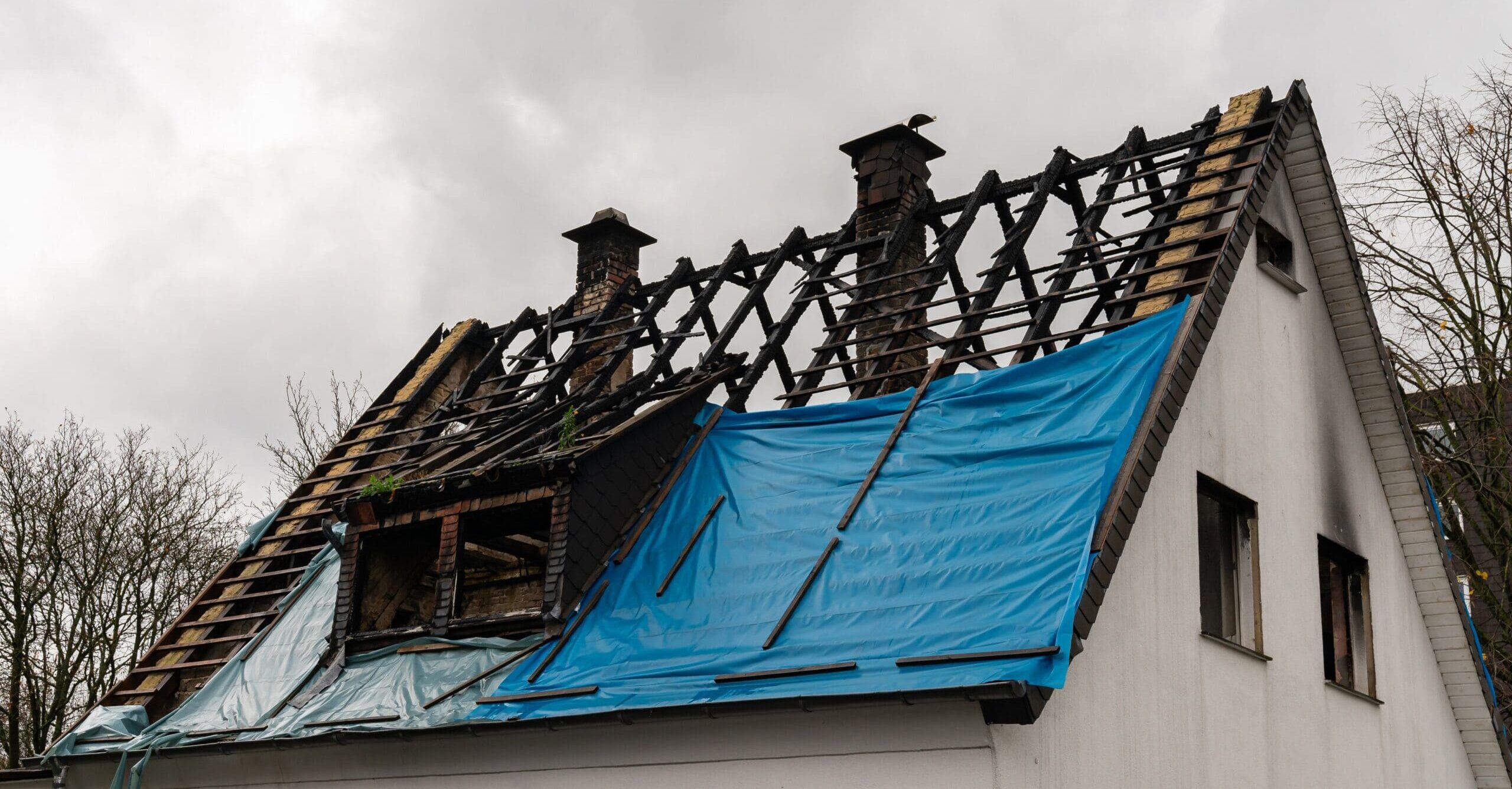 Fire damage visible on residential roof covered with blue tarp.