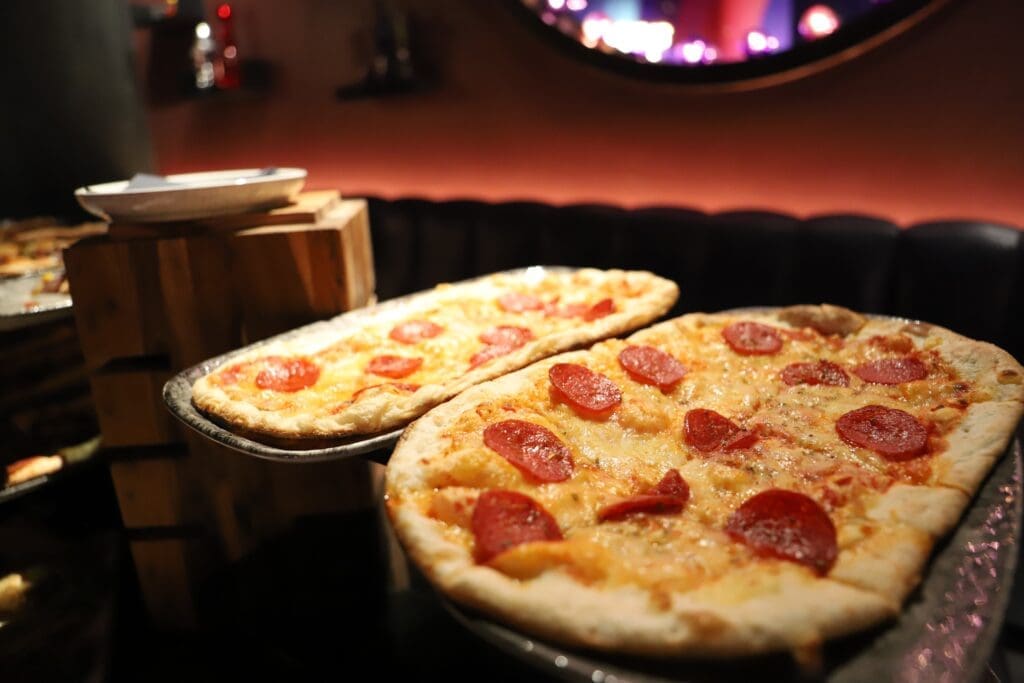 IMG_4417 - Lisa's Law Solicitors - Lisa's Law Solicitors Pepperoni pizzas on a metal tray in a dim restaurant, with a wooden stand and warm lighting.