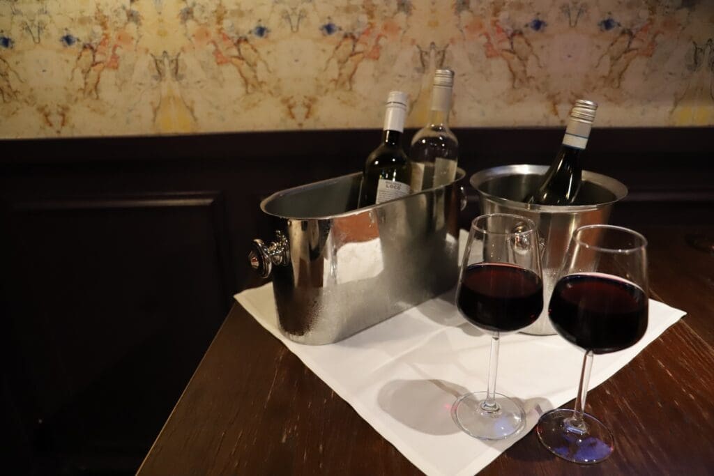 IMG_4425 - Lisa's Law Solicitors - Lisa's Law Solicitors Wine bottles chilling in a metal ice bucket with two glasses of red wine on a white napkin atop a wooden table.