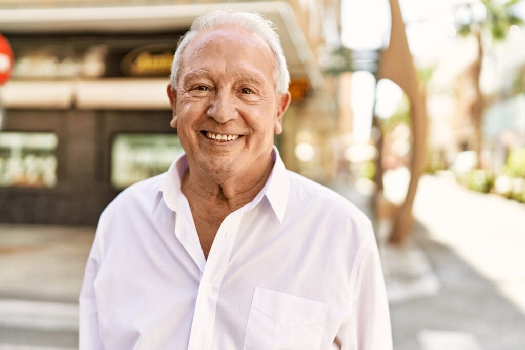 Senior man with grey hair standing happy outdoors on a sunny day.