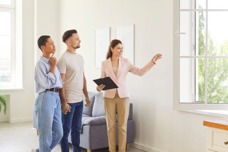 Female estate agent showing house to a young happy couple looking at the view from the window