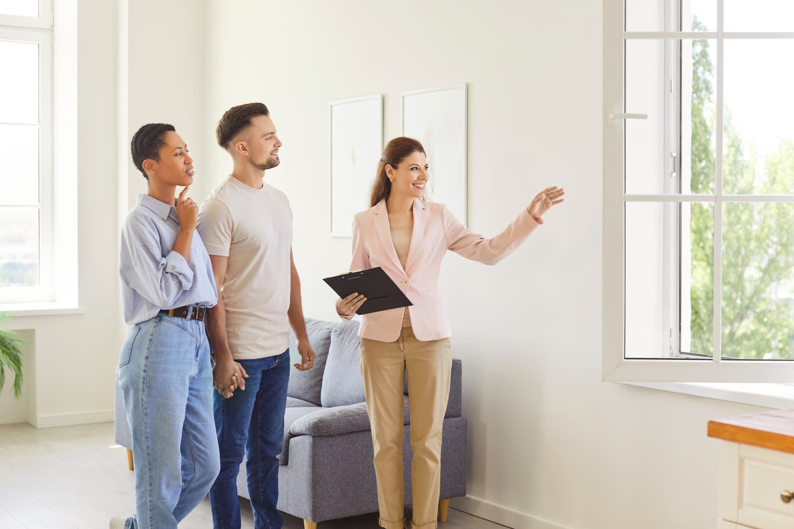 Female estate agent showing house to a young happy couple looking at the view from the window