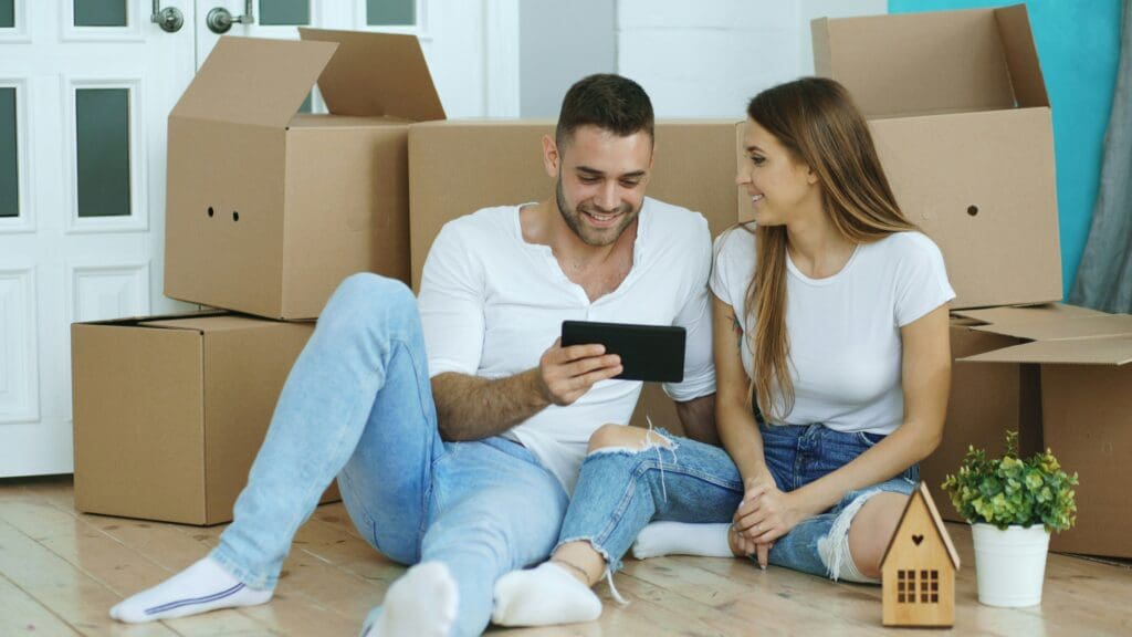 Young couple sitting on floor using tablet computer in their new house