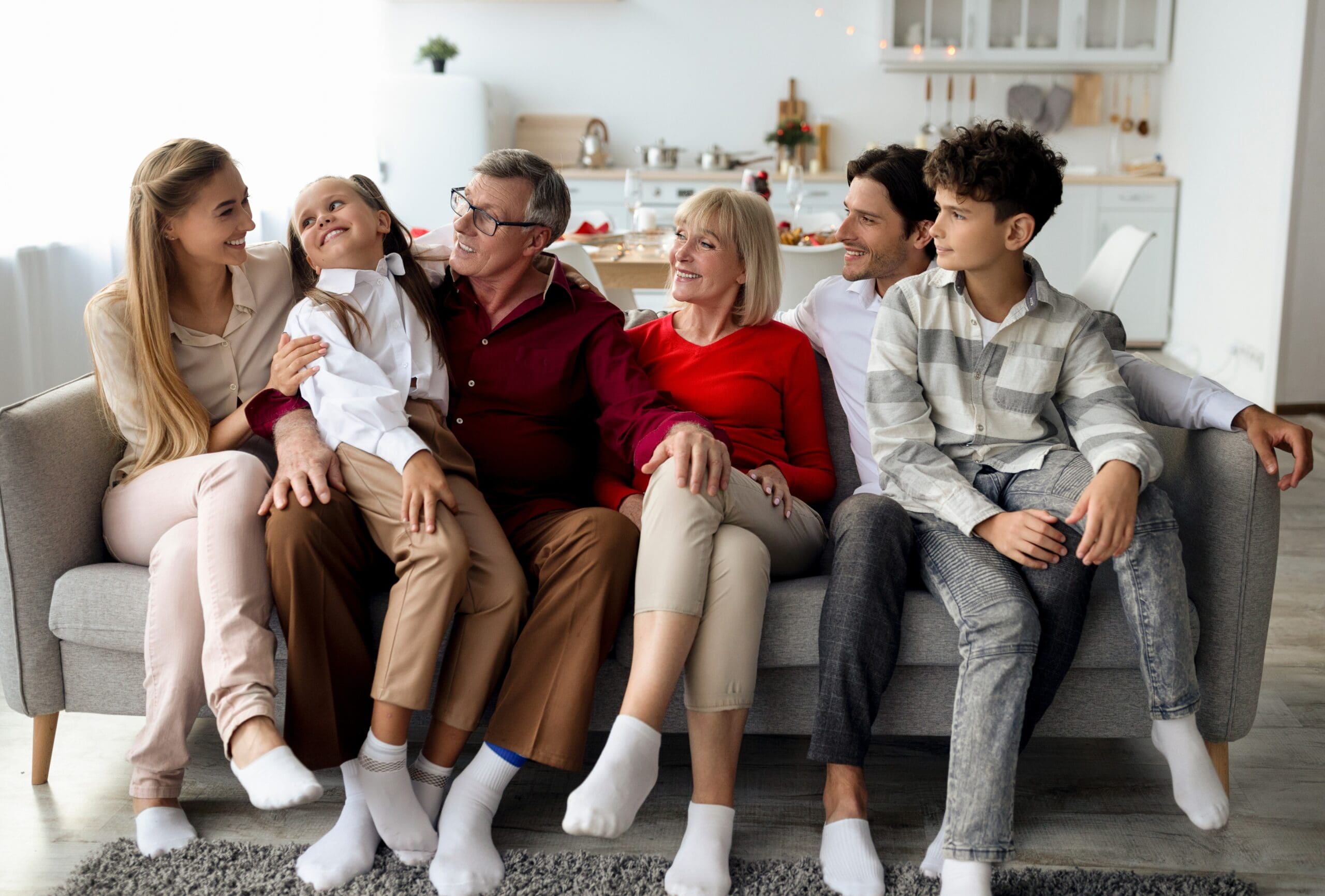 Big multi generation family with kids relaxing on sofa, smiling and chatting, spending bonding times together at home