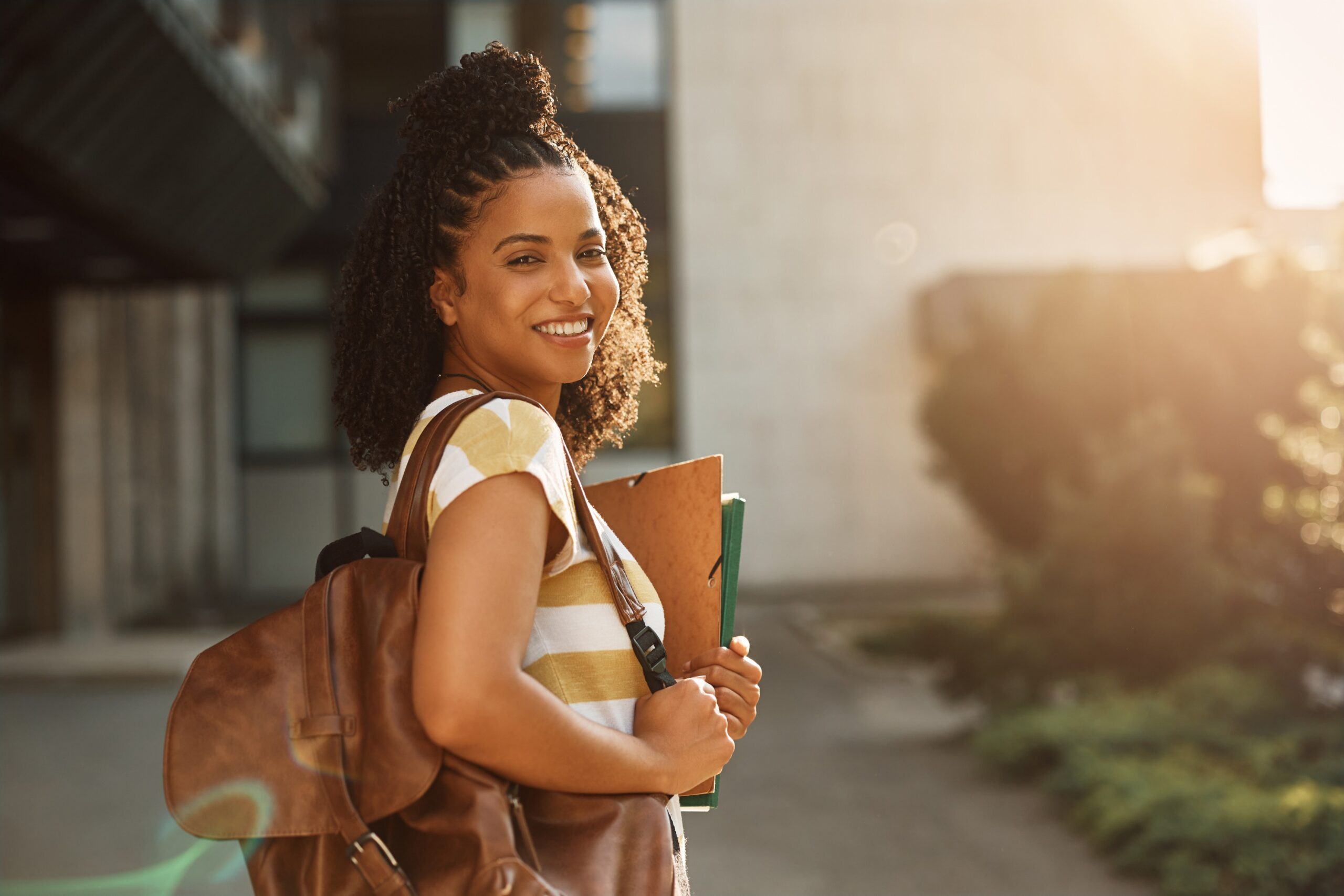 Happy African American female student in front of university building looking at camera.