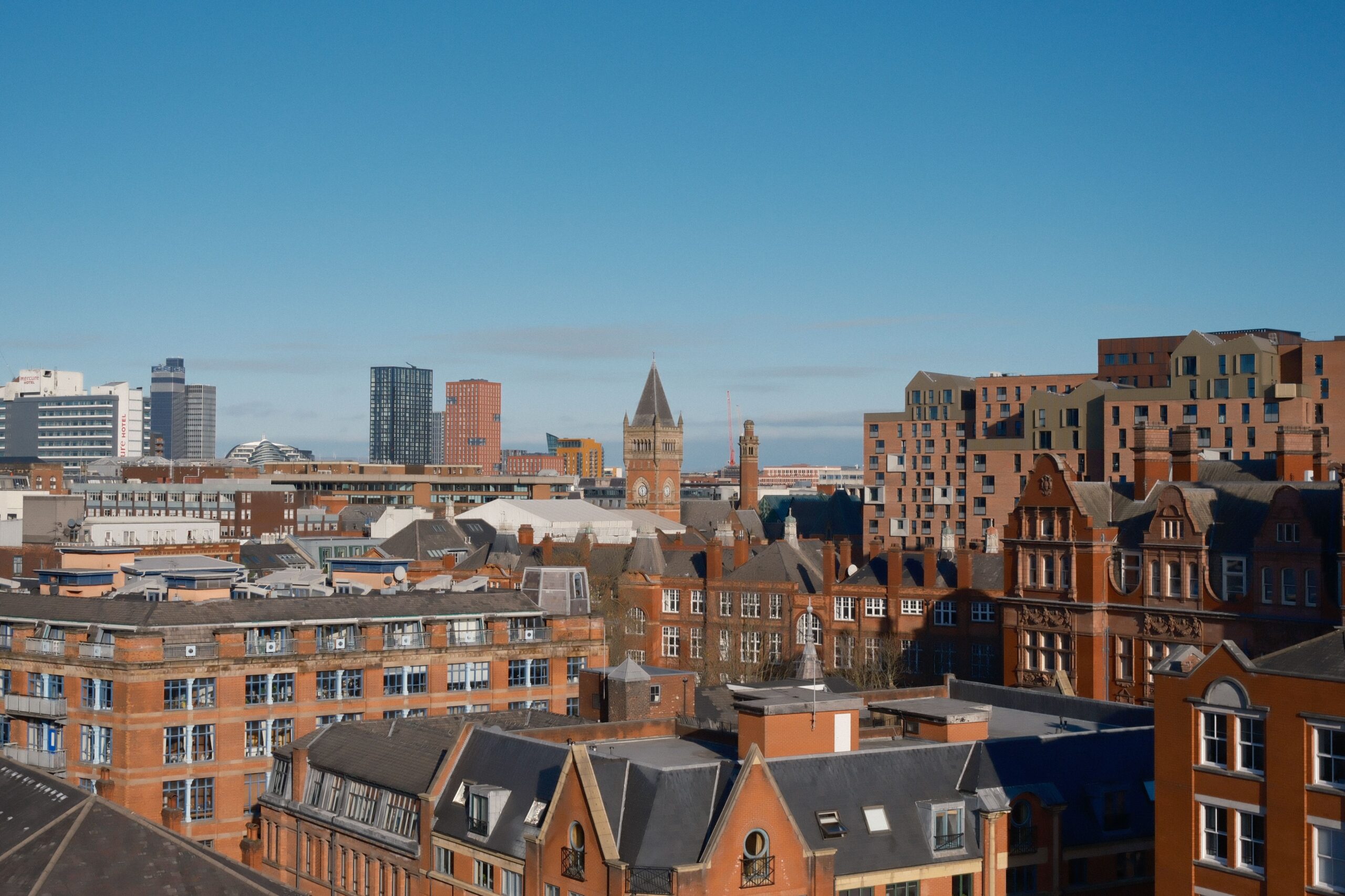City skyline with red brick buildings in foreground and modern office blocks against a clear blue sky.