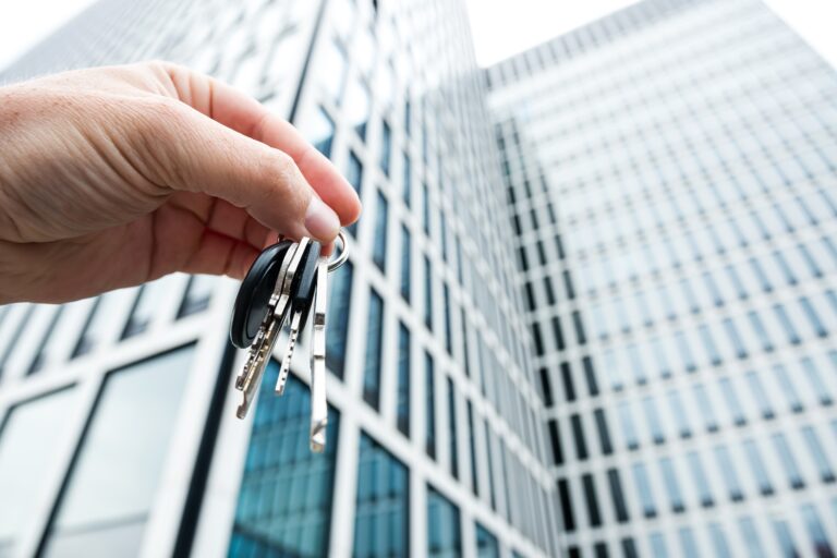 House keys in real estate agent against new skyscraper glass office. Concept buy or rent property