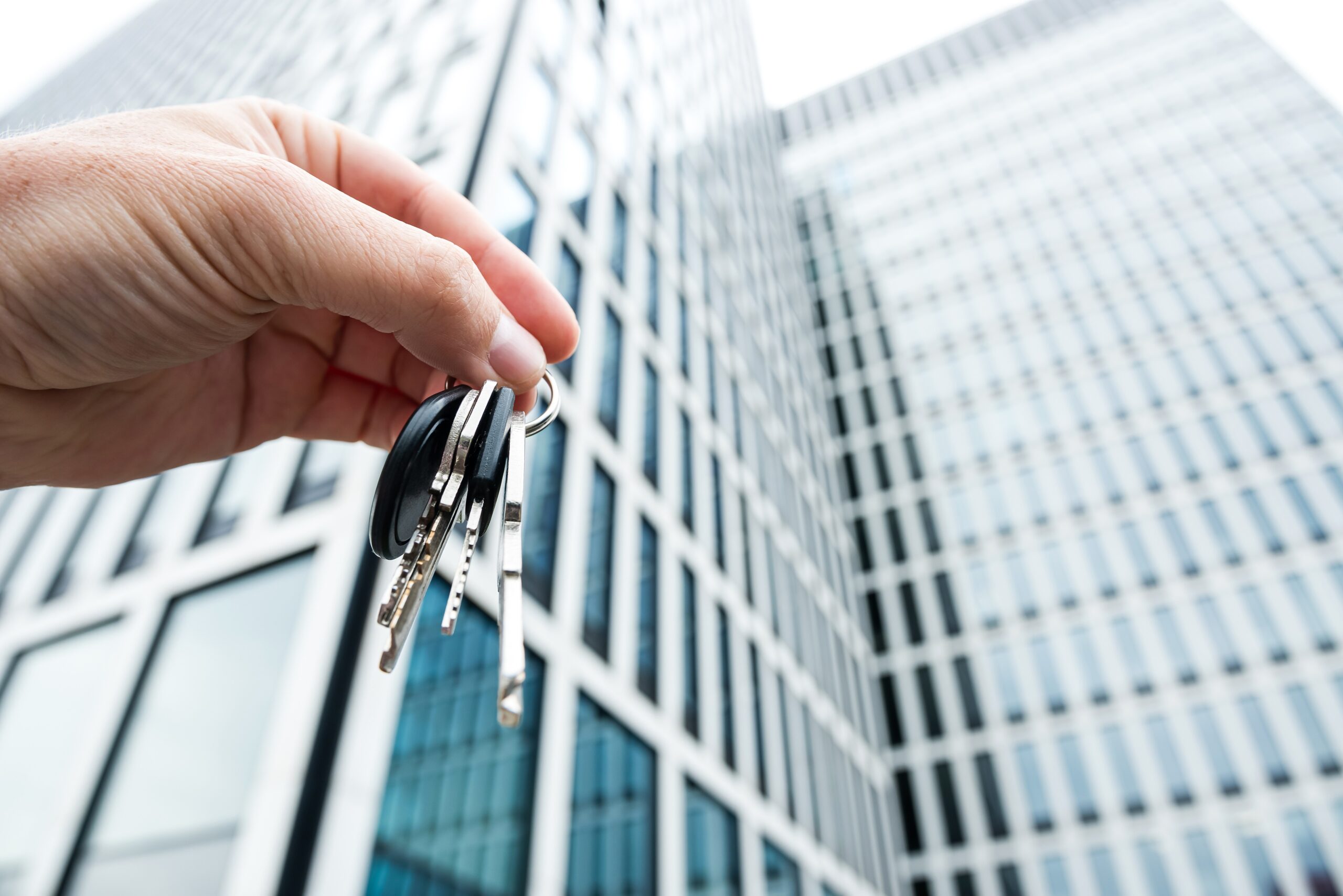 House keys in real estate agent against new skyscraper glass office. Concept buy or rent property